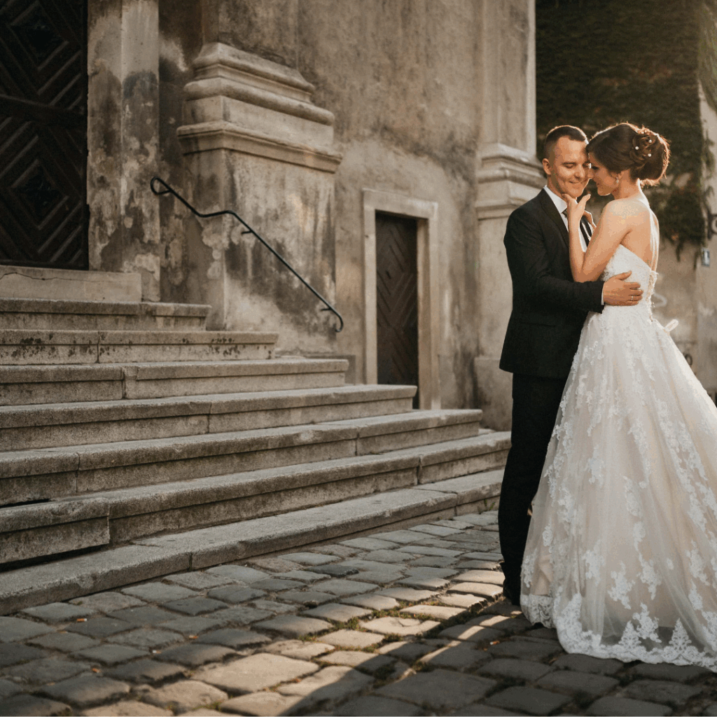 Bride and groom embracing on stone steps outside an old building.