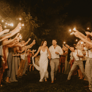 Bride and groom running through sparkler tunnel surrounded by guests at night.