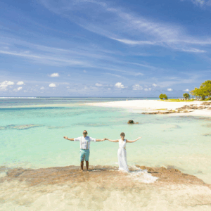 Couple holding hands on a tropical beach with clear water and blue sky
