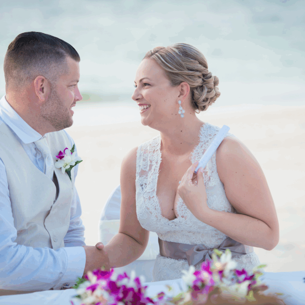 Bride and groom smiling at each other during a beachside wedding ceremony.